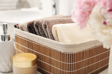 Soft towels in storage basket, peony flowers and cosmetic products on countertop indoors, closeupの写真素材