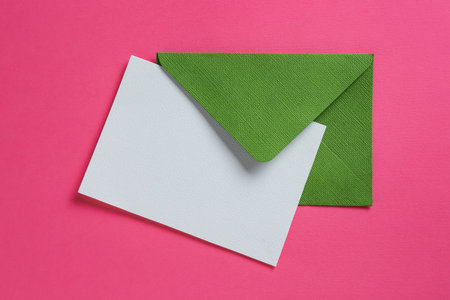 Blank invitation card and envelope on pink background, top view. Space for designの写真素材
