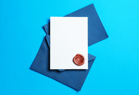 Blank invitation card with wax seal and envelopes on light blue background, flat lay. Space for designの写真素材