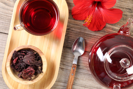 Delicious hibiscus tea in glass cup, teapot, dry roselle sepals and flower on wooden table, flat layの写真素材
