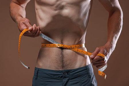Anorexic man measuring his waist on beige background, closeupのeditorial素材