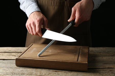 Man sharpening knife with sharpener on wooden table, closeupの写真素材