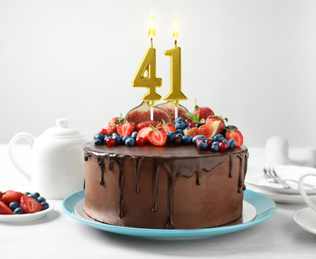 Yummy chocolate cake with fruits and burning number shaped candles on white table. 41th birthday or other special occasionの写真素材