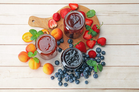 Different jams in jars and ingredients on white wooden table, flat lay