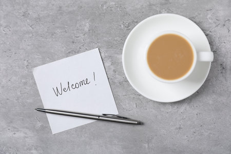 Sticky note with word Welcome, coffee and pen on grey table, flat layの写真素材