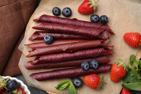 Tasty fruit leather rolls, strawberries, blueberries and mint on grey wooden table, flat layの写真素材