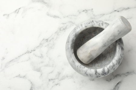 Mortar and pestle on white marble table, top view. Space for text