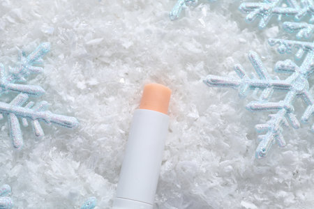 Moisturizing lip balm and Christmas decor on artificial snow, flat lay. Winter careの写真素材