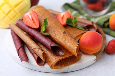 Delicious fruit leather rolls, mint, apricot, mango and strawberry on light table, closeup