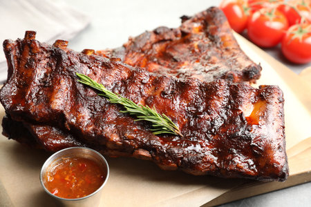 Tasty roasted pork ribs served with rosemary, tomatoes and sauce on light gray table, closeupの写真素材