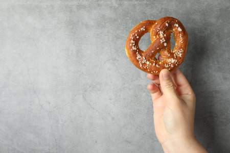 Woman with tasty pretzel near gray textured wall, closeup. Space for textの写真素材