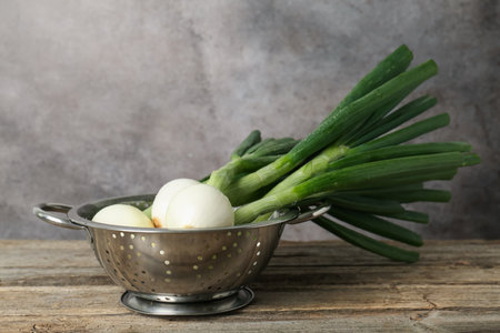 Fresh ripe green onions in colander on wooden table. Space for textの写真素材