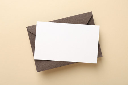 Blank invitation card and envelope on beige background, top view