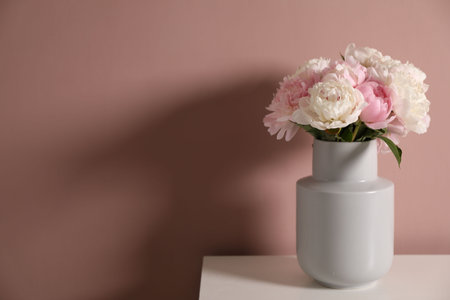 Beautiful peonies in vase on white table near pink wall. Space for textの写真素材