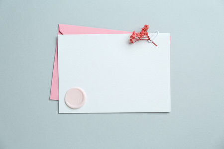 Blank invitation card with wax seal, flowers and envelope on gray background, top view. Space for designの写真素材