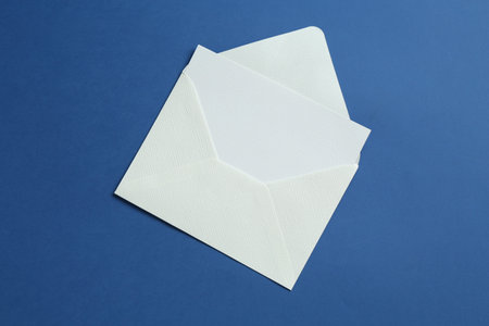 Blank invitation card and envelope on blue background, top view. Space for design