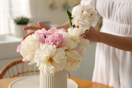 Woman making bouquet of beautiful peonies at table in kitchen, closeupのeditorial素材