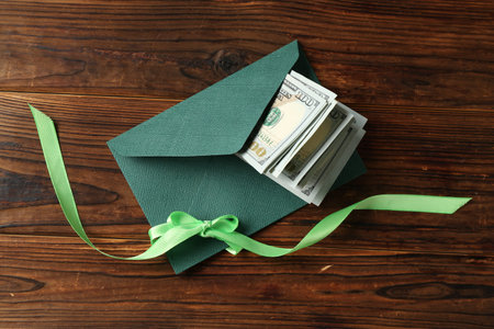 Money bonus. Envelope with dollar banknotes and ribbon on wooden table, top view