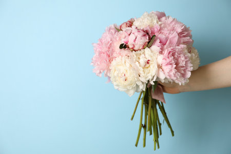 Woman holding bouquet of beautiful peonies on light blue background. Space for textのeditorial素材