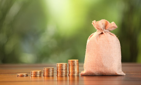 Burlap bag and stacked coins on wooden table against blurred backgroundの写真素材