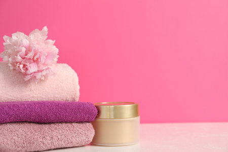 Soft towels, cosmetic product and peony flower on table against pink background, closeup. Space for textの写真素材