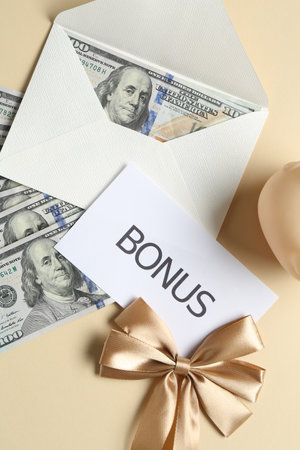 Card with word Bonus, envelope, dollar banknotes and bow on beige background, flat layの写真素材