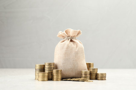 Bag and stacked coins on white table. Space for text
