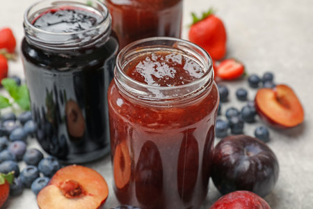 Different sweet jams in jars and ingredients on gray table, closeup