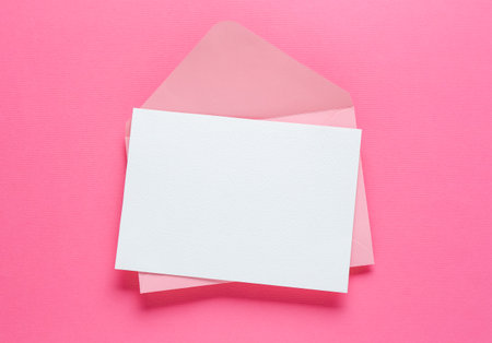 Blank invitation card and envelope on pink background, top view. Space for designの写真素材