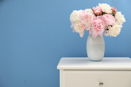 Beautiful peonies in vase on white dresser near light blue wall. Space for textの写真素材