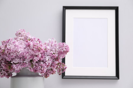 Beautiful lilac flowers in vase and picture frame on white background, closeupの写真素材