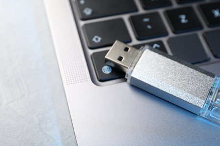 Flash drive and laptop on light gray table, closeup