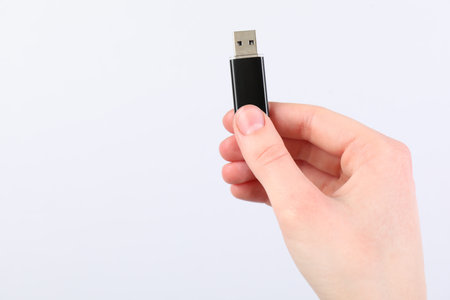 Man with modern flash drive on light gray background, closeup. Space for text