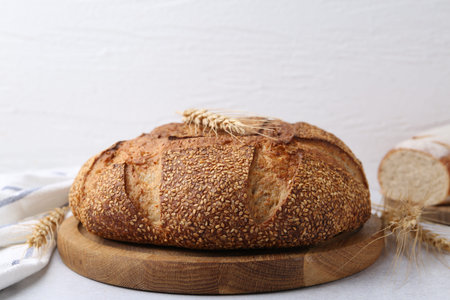 Freshly baked bread with sesame seeds and spikes on gray table against light background, closeup