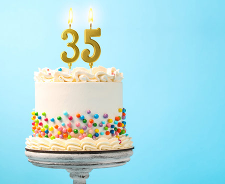 Yummy cake with sprinkles and burning number shaped candles on light blue background, space for...