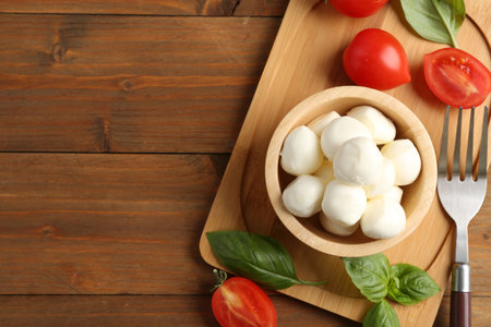 Tasty mozzarella balls, tomatoes and basil on wooden table, flat lay. Space for text