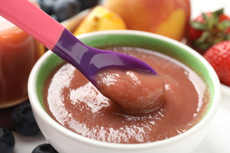 Baby food. Eating tasty puree with spoon at white table, closeupの写真素材