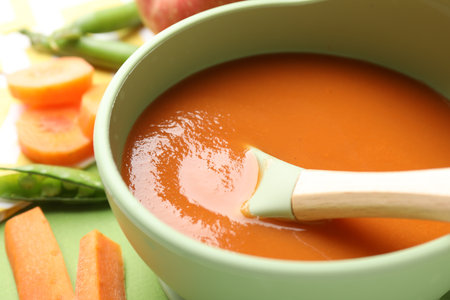 Baby food. Tasty puree in bowl and ingredients on green background, closeupの写真素材