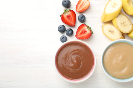 Baby food. Tasty puree in bowls and different ingredients on white wooden table, flat layの写真素材