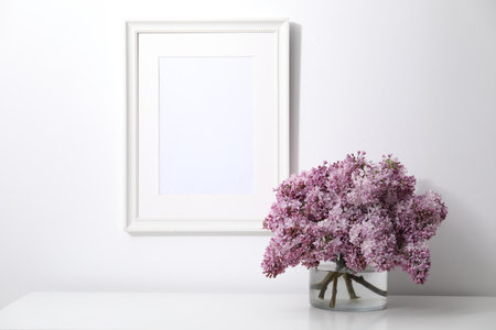 Beautiful lilac flowers in glass vase on table and picture frame indoorsの写真素材