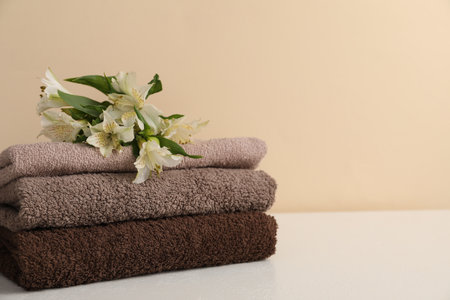 Stack of soft towels and lilies on white table against beige background, closeup. Space for textの写真素材