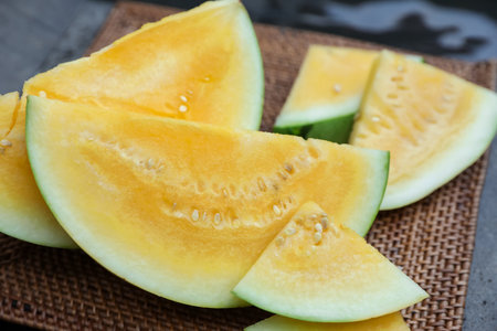 Pieces of ripe yellow watermelon on wicker table near swimming pool, closeupの写真素材