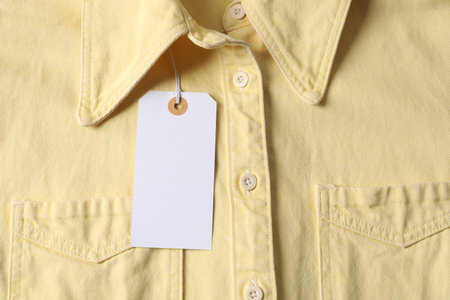 Cardboard tag on pale yellow shirt, top viewの写真素材