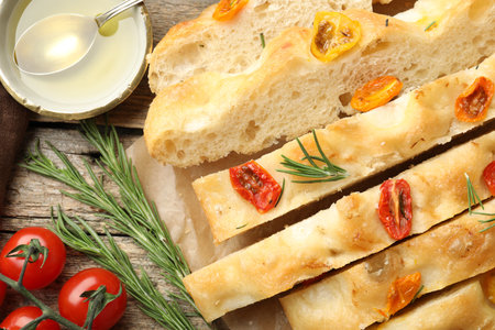 Cut delicious focaccia with tomatoes, spices and oil on wooden table, flat layの写真素材