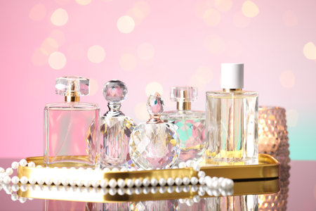 Many different perfume bottles and accessories on mirror surface against pink background with blurred lights, closeupの写真素材