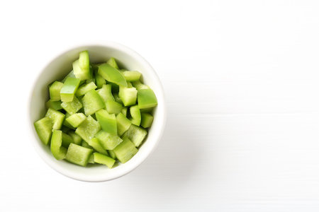 Pieces of fresh green bell pepper in bowl on white wooden table, top view. Space for textの写真素材