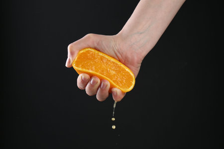 Woman squeezing orange on black background, closeupの写真素材