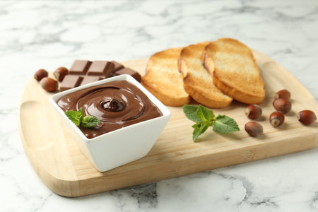 Tasty chocolate spread, pieces, toasts, mint and hazelnuts on white marble table, closeupの写真素材