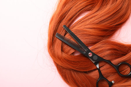 Hair strand and scissors on light pink background, top view. Space for textの写真素材