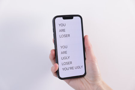 Cyber bullying. Woman holding smartphone with insults on light background, closeupのeditorial素材
